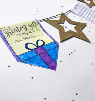 A hand-drawn gift tag reading “The greatest gift in my life is my family” sits beside a blue present with a purple bow—part of the Christmas Writing Activity | Sharing My Gifts Pennant Banner Craft by Differentiated Teaching with Rebecca Davies.